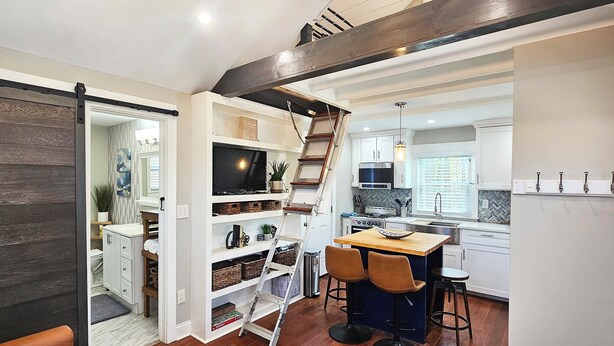 A modern kitchen with a wooden staircase, built-in shelves, and a dining area with a wooden table and chairs. - Private Atlanta Tiny House with 
Mini Golf Course (Forest Park)