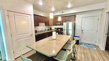 A modern kitchen with a central island, bar stools, stainless steel appliances, and wooden flooring.