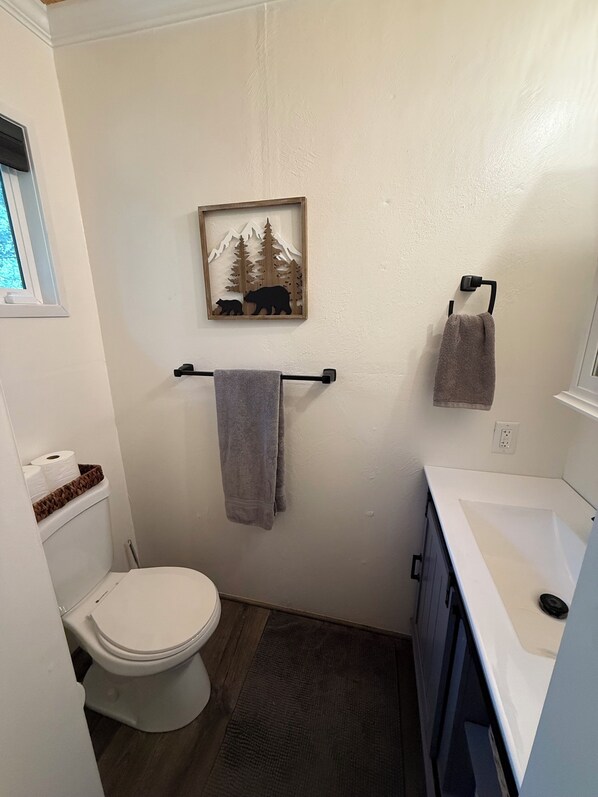 A small, clean bathroom with a toilet, a towel rack, and a framed picture of a bear and trees on the wall. - Family Cabin Near Bass Lake & Yosemite, Sleeps 12 + Kids’ Game Loft (Wishon)