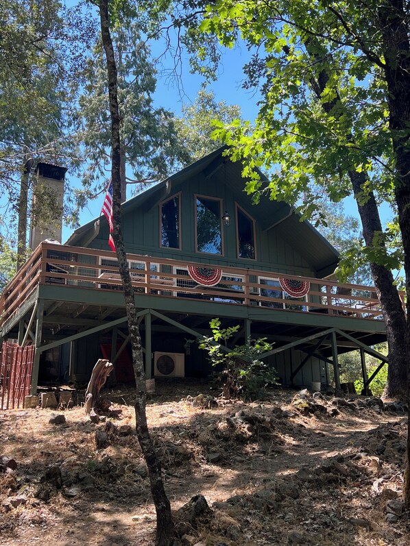 A rustic cabin with a wooden deck, large windows, and an American flag.