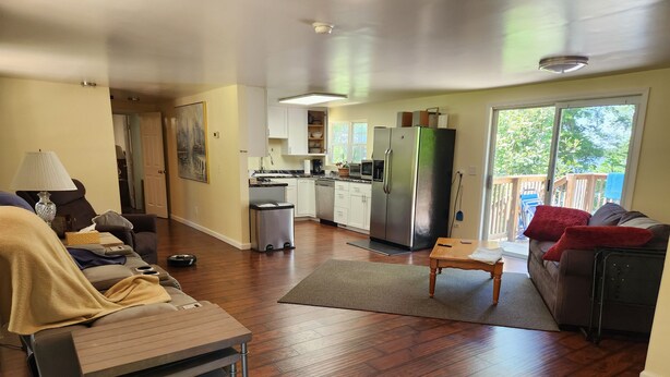 Amplia sala de estar con piso de madera, comedor y cocina con refrigerador grande.