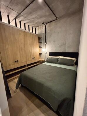 Quarto com cama, guarda-roupa de madeira e mesa de cabeceira.