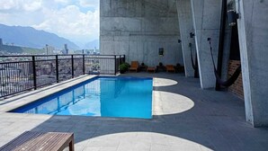Una piscina sul tetto con vista sulle montagne, una struttura in cemento e una panchina di legno.