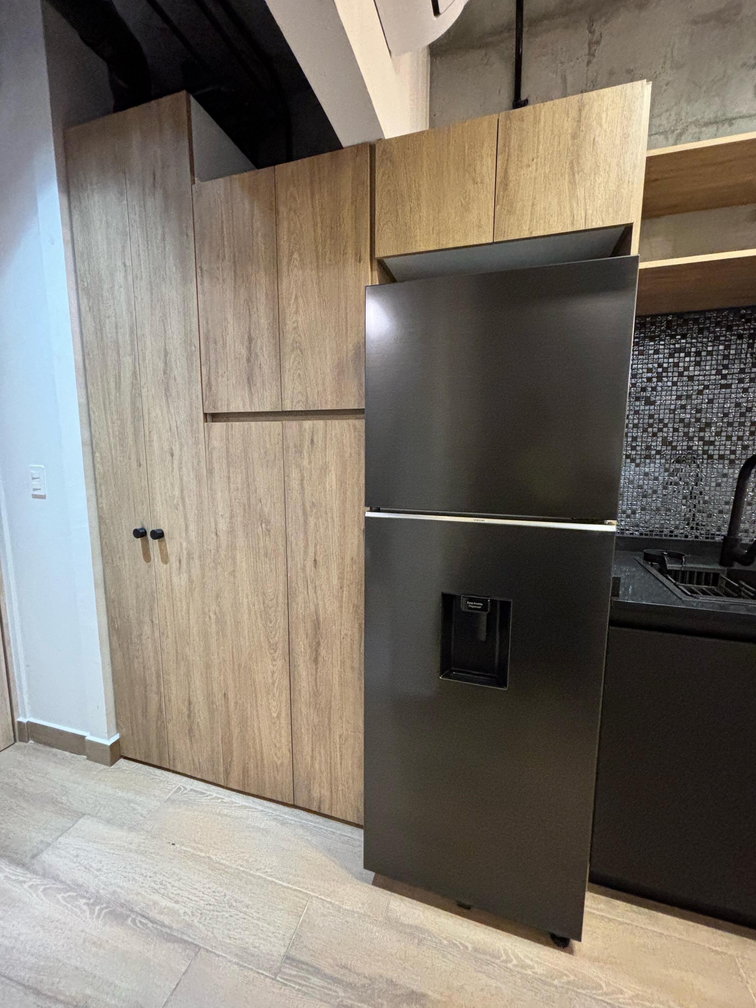 A kitchen with a stainless steel refrigerator, wooden cabinets, and a tiled backsplash.
