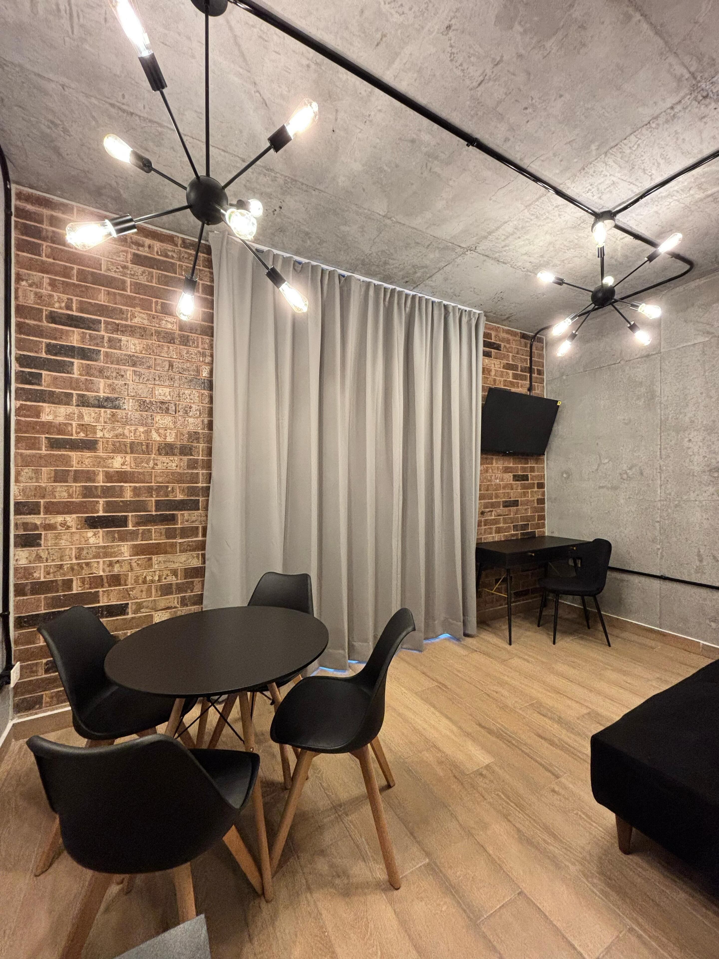 Quarto moderno com parede de tijolos, mesa redonda com cadeiras, sofá preto e ventilador de teto.