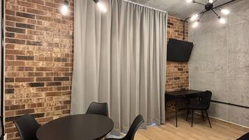 Quarto moderno com parede de tijolos, mesa redonda com cadeiras, sofá preto e ventilador de teto.