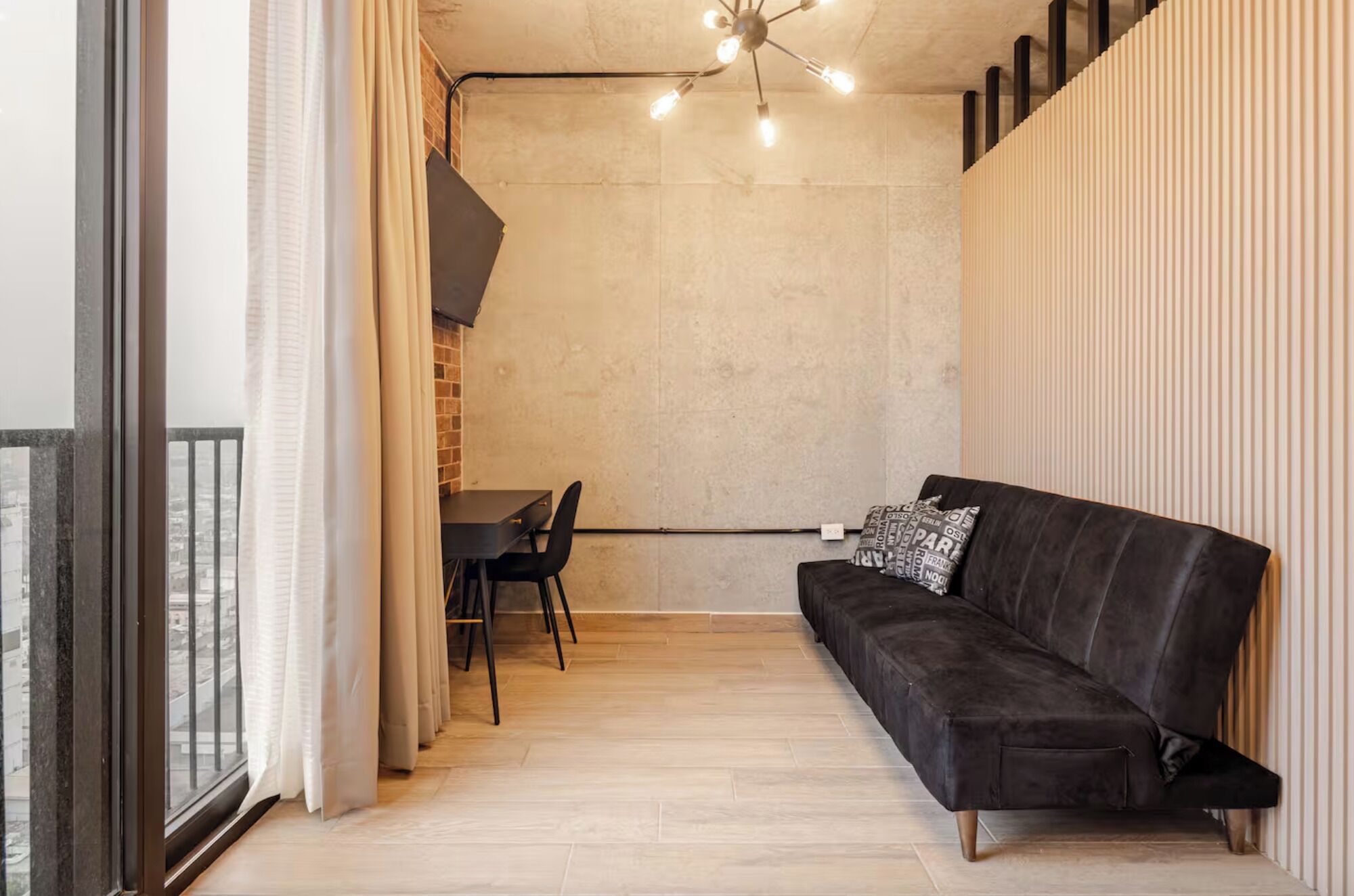 A modern living space with a black sofa, a dining table with chairs, and a ceiling light fixture.