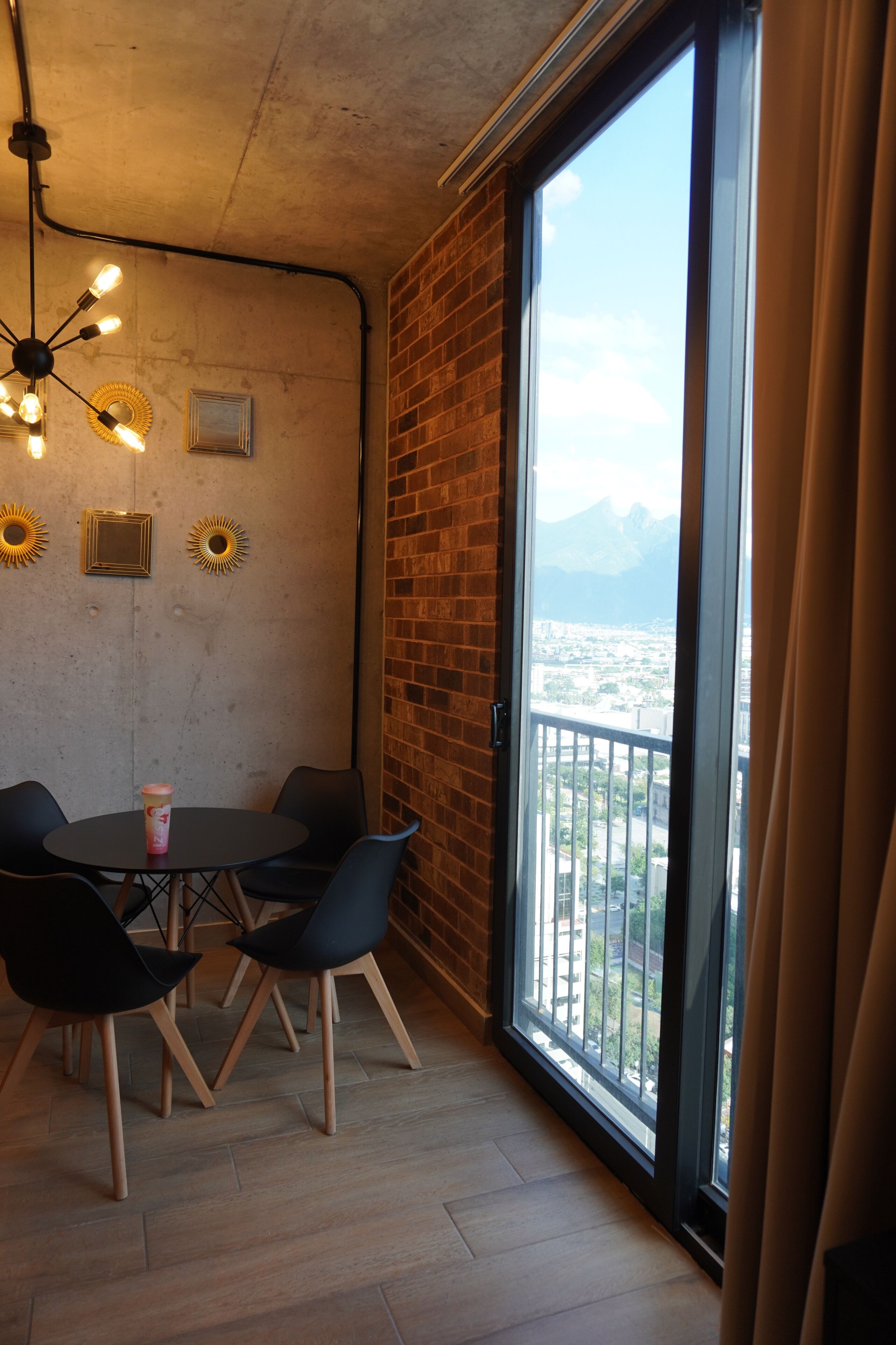 A room with a large window, a round table with chairs, and a ceiling light fixture.