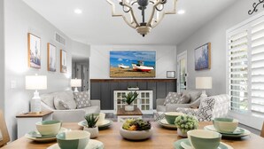 A modern living room with a dining area, featuring a chandelier, sofas, a coffee table, and a large flat-screen TV mounted on the wall. - Family Paradise-Kid and Pet Friendly Home by Encanto Golf Course-Downtown  Phx. (Phoenix)