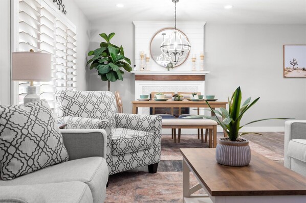 Un salon moderne avec un fauteuil à motifs, une table à manger avec des chaises, une table basse, une plante en pot et un lustre.