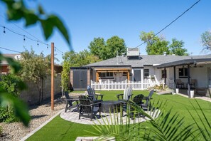 Une maison dotée d’un patio aménagé avec du mobilier d’extérieur, une clôture blanche en bois et une pelouse bien entretenue.