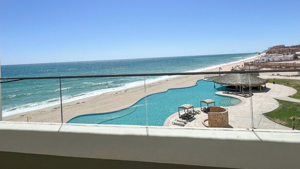 A pool area with a beach view, including a swimming pool, lounge chairs, and a thatched-roof structure. - Barcelona 307 Ocean Front Brand New 3-bedroom condo. WiFi in lovely Las Palomas (Puerto Peñasco)