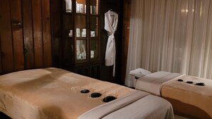 A spa room with two massage tables, a wooden cabinet with bottles, and a white robe hanging on the wall. - The best room to relax (Nanoose Bay)