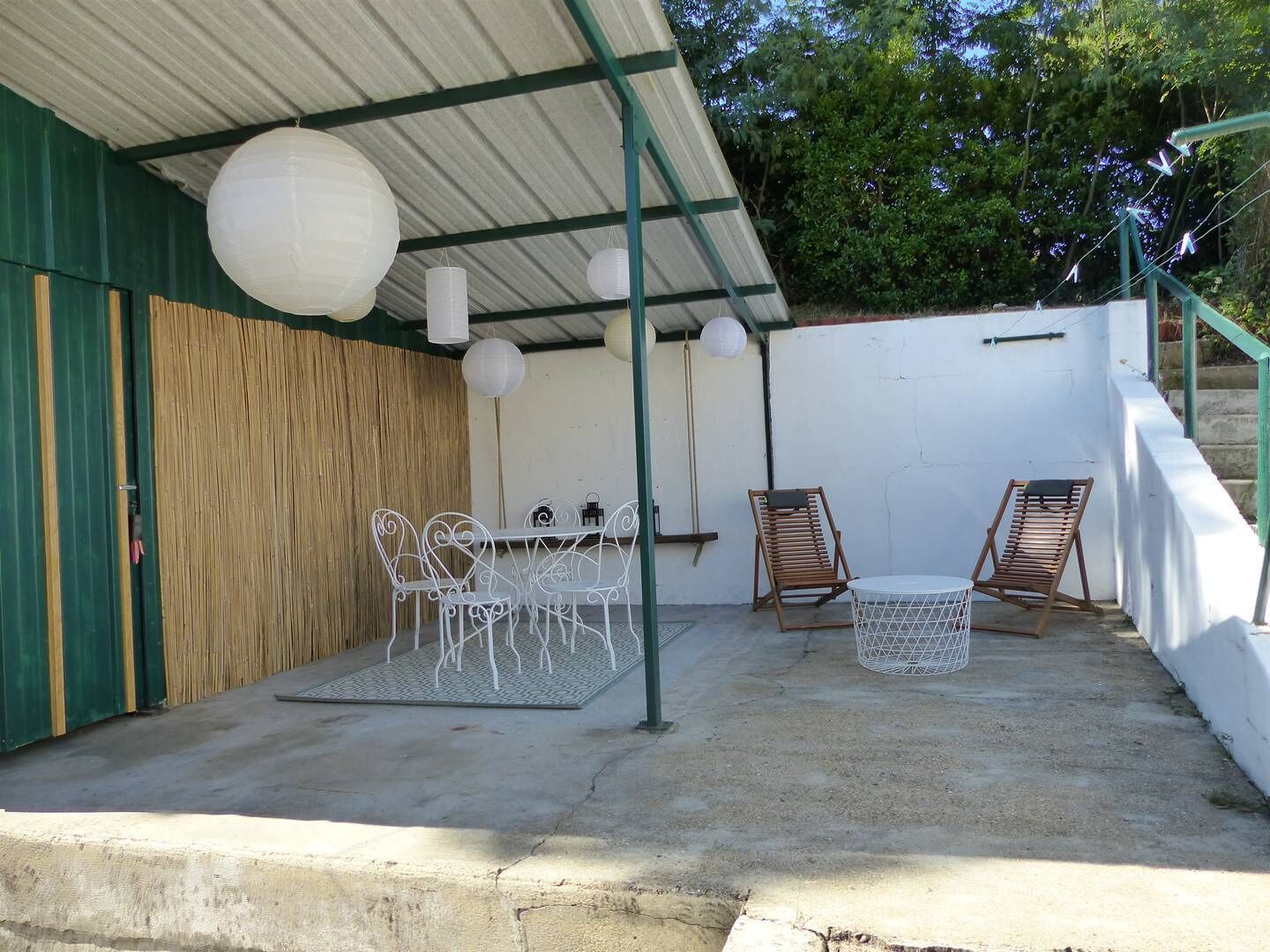 An outdoor patio with a table and chairs, surrounded by a wooden fence and a white wall.