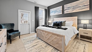 A bedroom with a bed, a chair, a nightstand, a ceiling fan, and artwork on the wall. - The Journey Home | JZ Vacation Rentals (St. Louis)