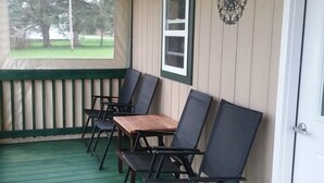 Een overdekte veranda met vier zwarte stoelen en een houten tafel, een witte deur en een raam met uitzicht op bomen.