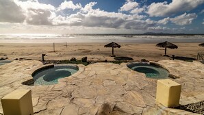 Un espace piscine en pierre avec deux bains à remous, une vue sur la plage et un ciel dégagé.