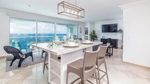 Une cuisine moderne dotée d’un grand îlot central, de meubles blancs et offrant une vue sur l’océan.