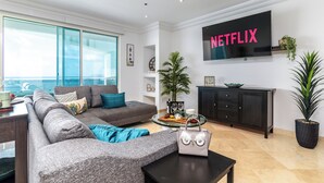 Un salon moderne avec un canapé gris, une table basse et un téléviseur affichant le logo « NETFLIX ».