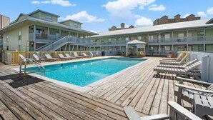 Zona de piscina con muelle de madera, sillas de descanso y un edificio con balcones.