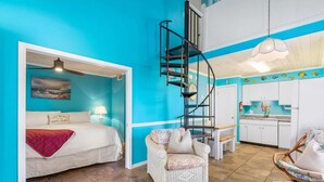 Una habitación con cama, una silla, una mesita, una escalera de caracol y una zona de cocina.