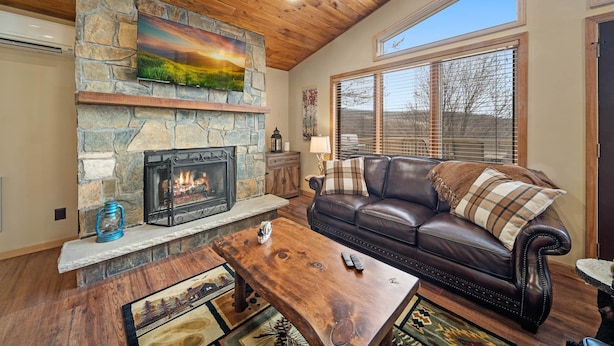 A cozy living room with a stone fireplace, leather sofa, and a wooden ceiling. - Spacious 6BR mountain retreat with hot tub, game room, and views. (Beech Mountain)
