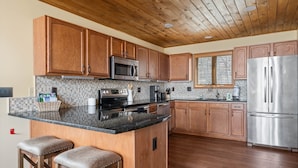 A kitchen with wooden cabinets, a stainless steel refrigerator, a microwave, and a coffee maker. - Spacious 6BR mountain retreat with hot tub, game room, and views. (Beech Mountain)