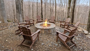 A circular fire pit with chairs around it in a forest setting. - Spacious 6BR mountain retreat with hot tub, game room, and views. (Beech Mountain)