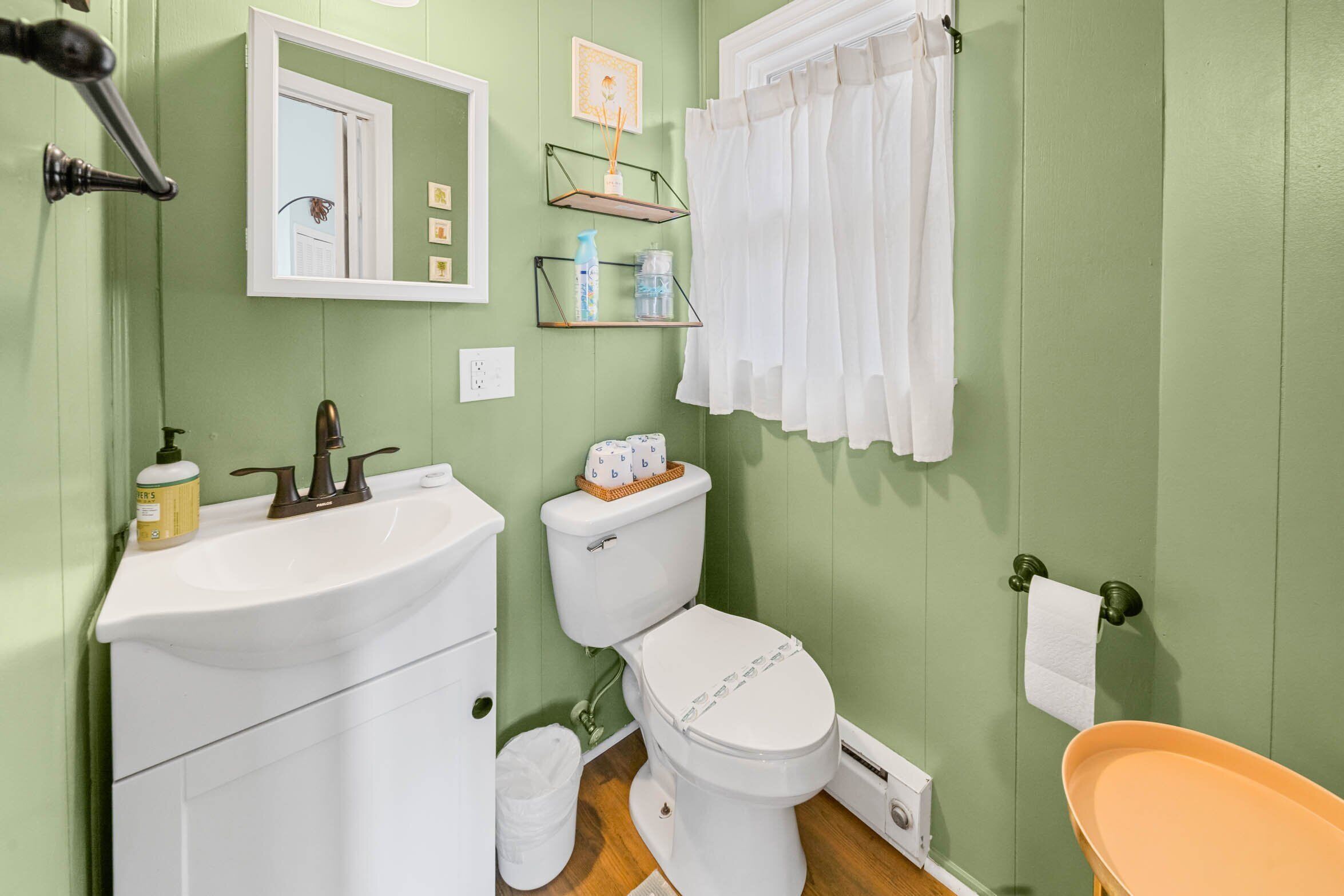 A bathroom with a white sink, toilet, and bathtub. There are shelves above the toilet and a mirror on the wall.