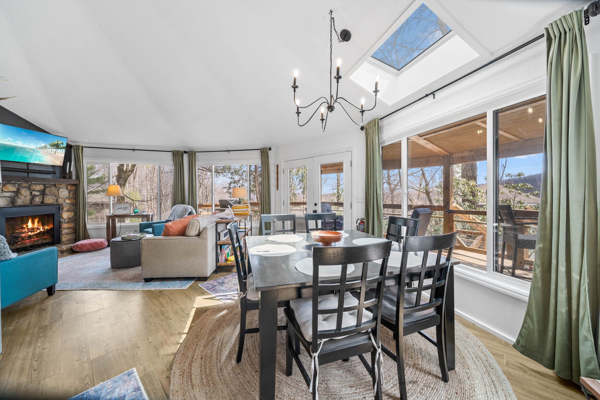 A spacious living area with a fireplace, a dining table, and a large window offering a view of the outdoors.