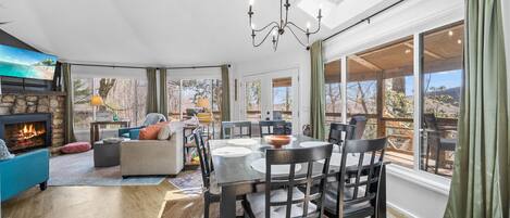 A spacious living area with a fireplace, a dining table, and a large window offering a view of the outdoors.