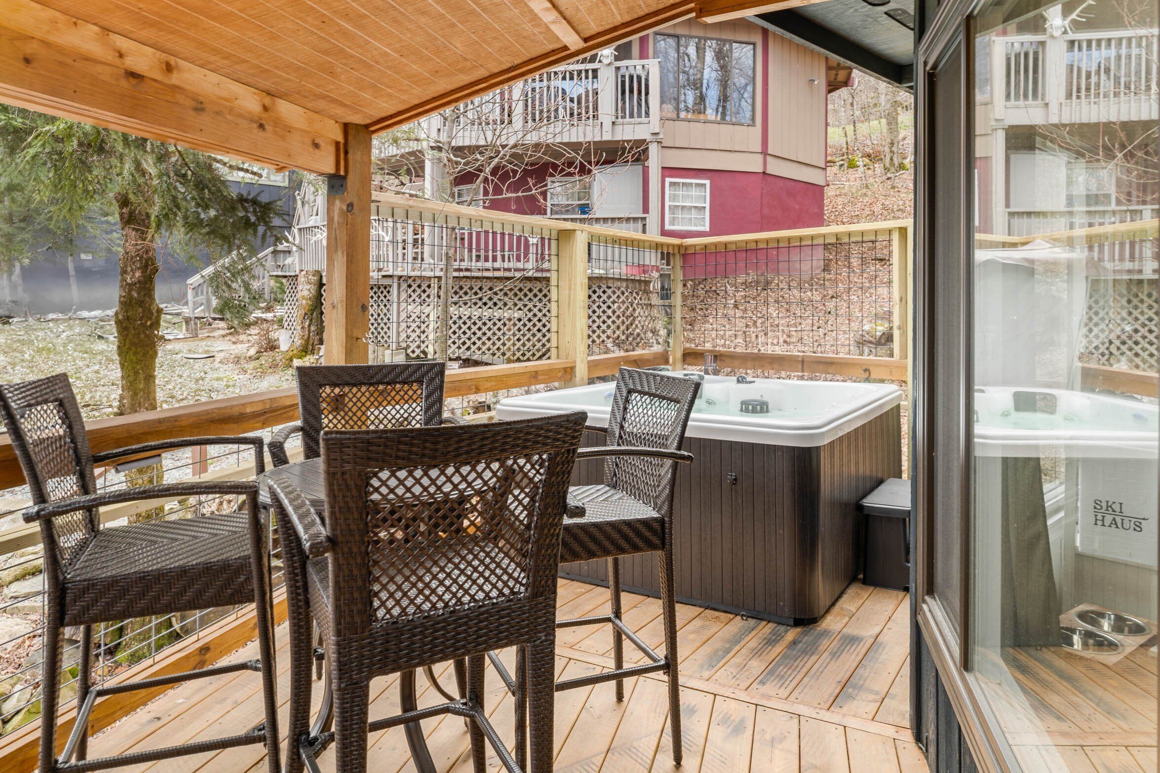 A covered outdoor area with wicker furniture, a hot tub, and a view of a building with balconies.