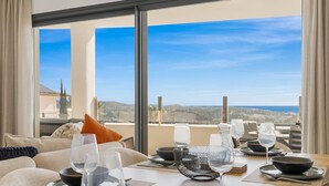 A dining area with a table set for two, large windows with a view of the landscape, and a sofa with cushions. - Mariposa | Sea view - pool - terrace - spa (La Cala de Mijas)