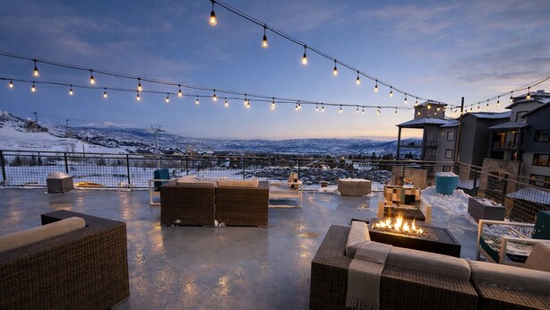 A rooftop patio with wicker furniture, a fire pit, and string lights against a snowy mountain backdrop. - Ski-Access  2 Queen Beds  Private Patio  Hot Tub (Park City)
