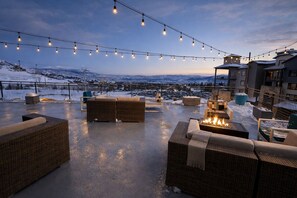 Un patio en la azotea con mobiliario de mimbre, un brasero y luces colgantes, con una imponente montaña nevada al fondo.
