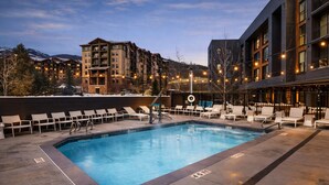 A pool area with lounge chairs and a pool, surrounded by buildings with balconies and lights. - Ski-Access  2 Queen Beds  Private Patio  Hot Tub (Park City)