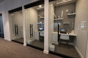 A modern office space with glass partitions, white desks, and built-in shelving.