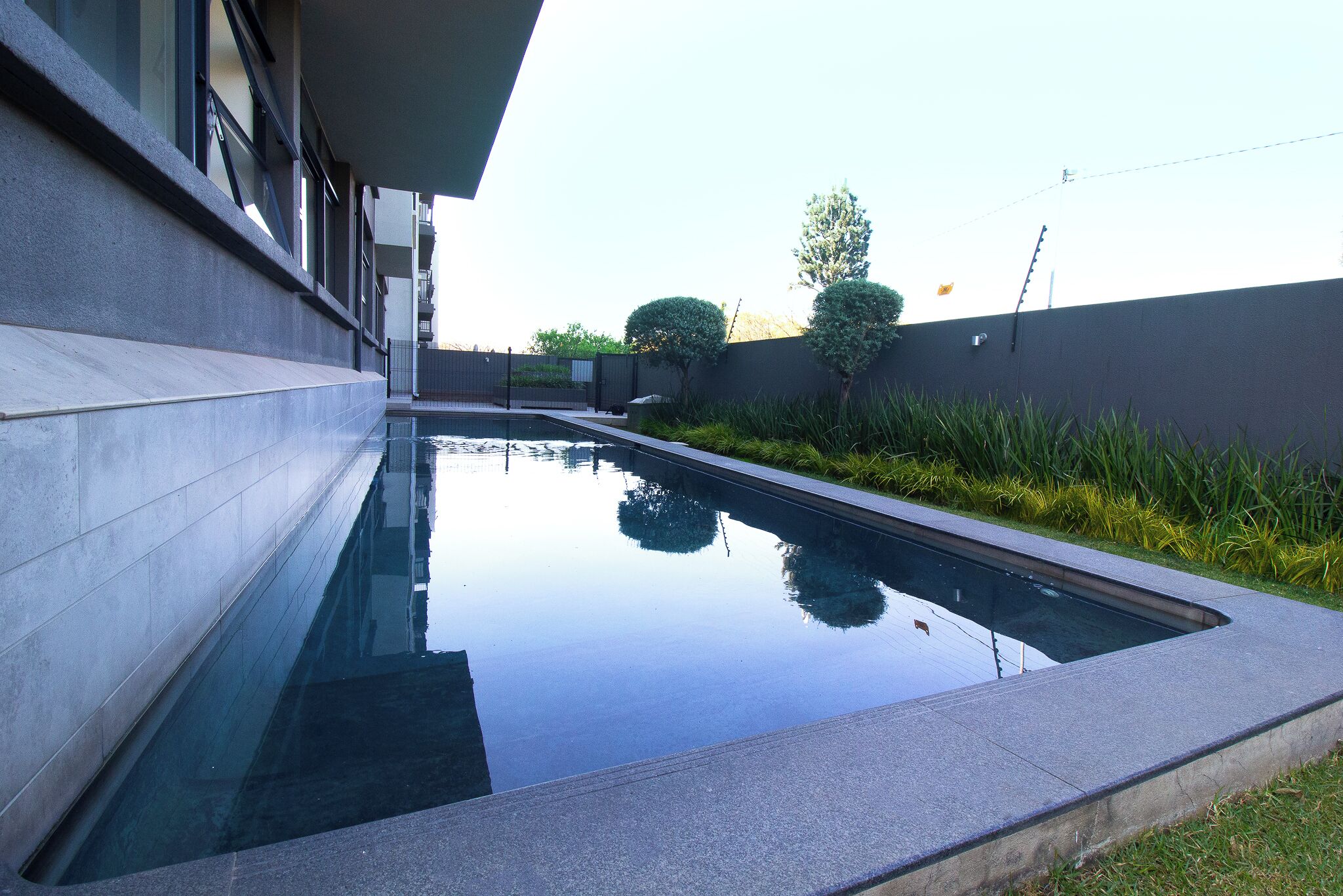 Une piscine moderne au design géométrique, entourée d’un petit muret et d’une zone herbeuse.