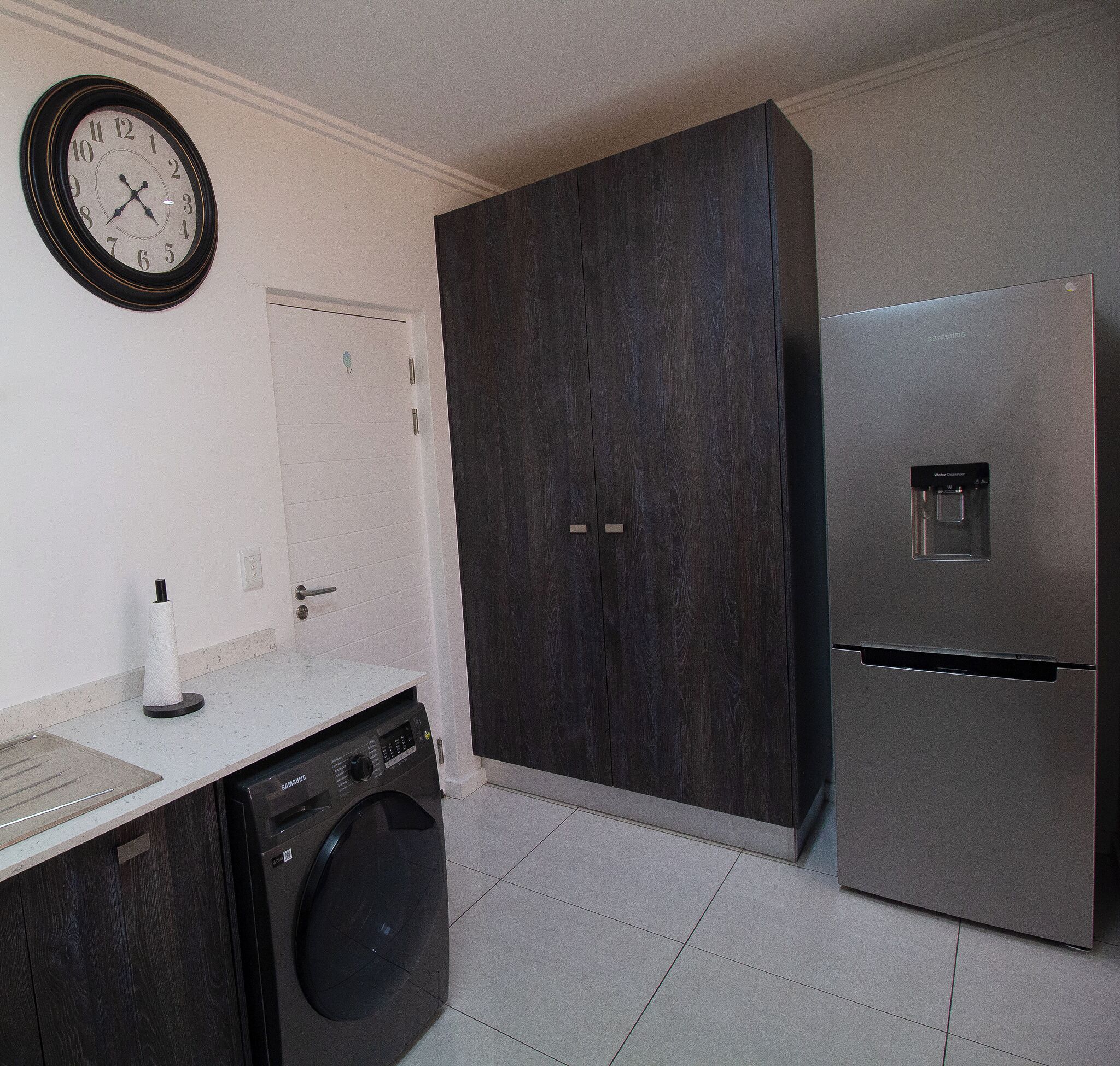 A modern kitchen with a washing machine, a refrigerator, and a clock on the wall.