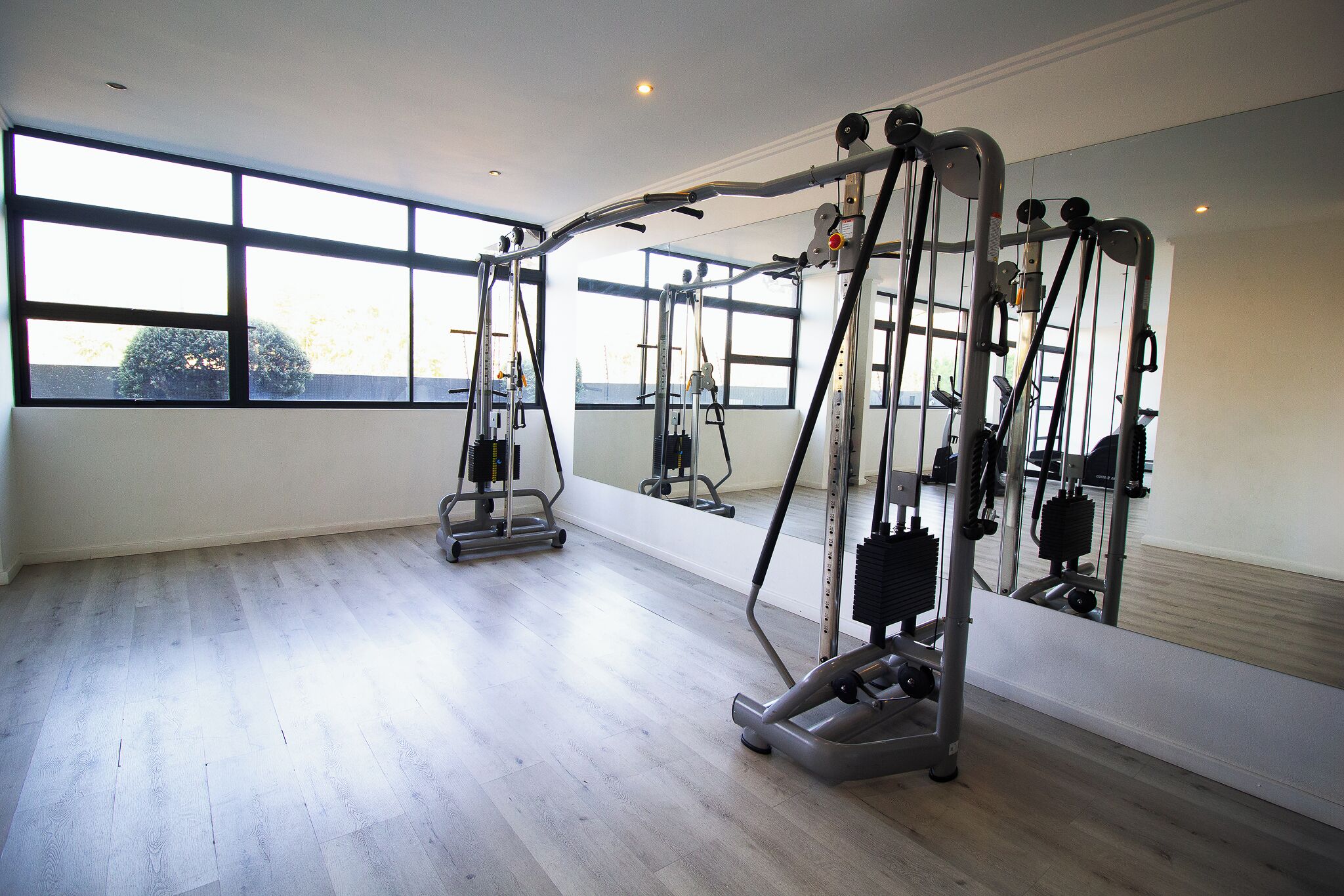 Ein Fitnessraum mit Trainingsgeräten, großen Fenstern und Holzboden.