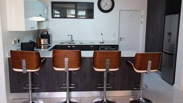 A modern kitchen with a central island, bar stools, a clock, and a refrigerator.