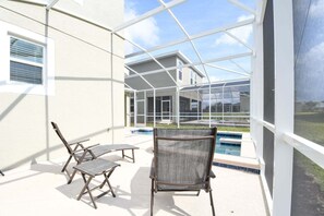 A covered patio with two chairs, a pool, and a house in the background. - Champions Gate Gem – Pool, Spa, Near Parks (Davenport)