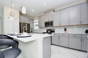 A modern kitchen with grey cabinets, a central island, stainless steel appliances, and a dining area with chairs. - Champions Gate Gem – Pool, Spa, Near Parks (Davenport)