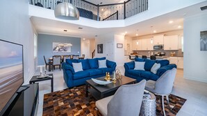 Un vaste espace de vie comprenant deux canapés, une table basse et un téléviseur. Un escalier mène à l’étage supérieur.