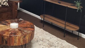 Ein Wohnzimmer mit rundem Couchtisch, einer Couch, einem an der Wand montierten Fernseher und einer kleinen Pflanze auf einem Regal.