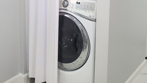 Eine kompakte, wäschebehälterlose Waschmaschine in einem kleinen Waschraum mit weißen Wänden und Marmorböden.