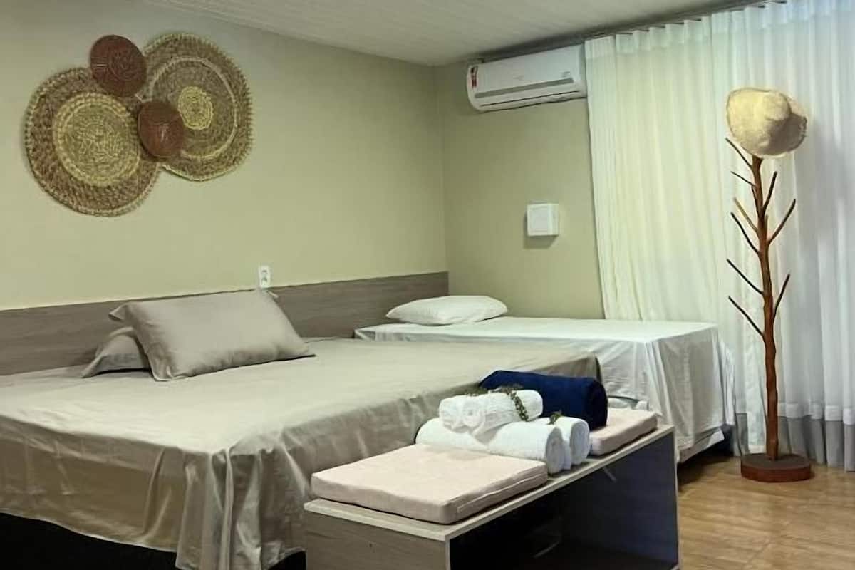 A hotel room with two beds, a small table, a wall-mounted air conditioner, and a decorative wall hanging.