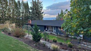 A modern house with a dark roof, surrounded by a well-maintained garden and tall trees.