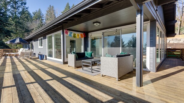 A modern house with a covered patio, outdoor furniture, and a view of the surrounding forest.