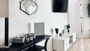 Un salon moderne avec une console noire, un miroir aux motifs géométriques, un téléviseur à écran plat et un meuble blanc.